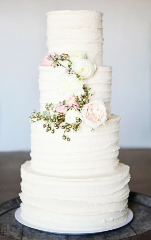 a white textural buttercream wedding cake decorated with white and blush blooms and gold berries looks amazing