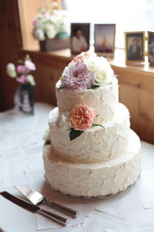 a white textural buttercream wedding cake topped with white, lilac and peachy blooms and greenery is great for spring and summer