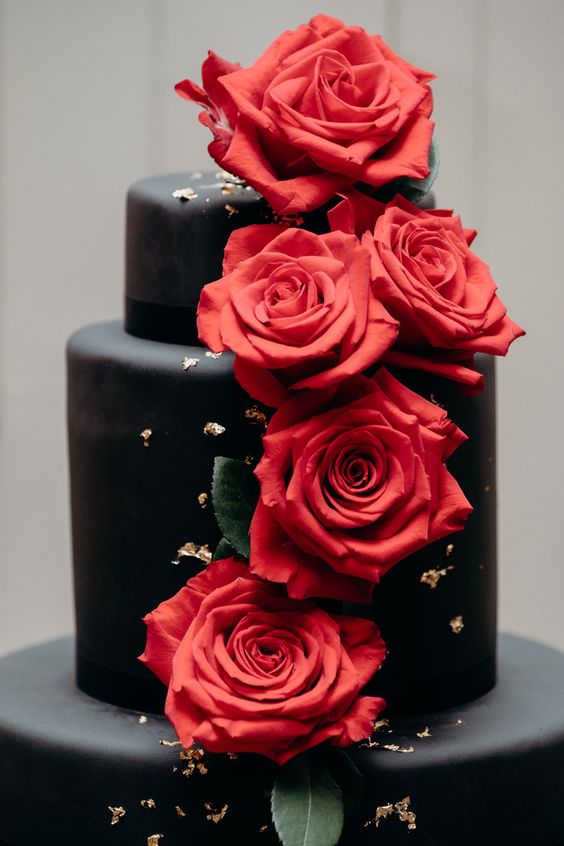 a black wedding cake decorated with red roses and gold leaf is a chic modern idea
