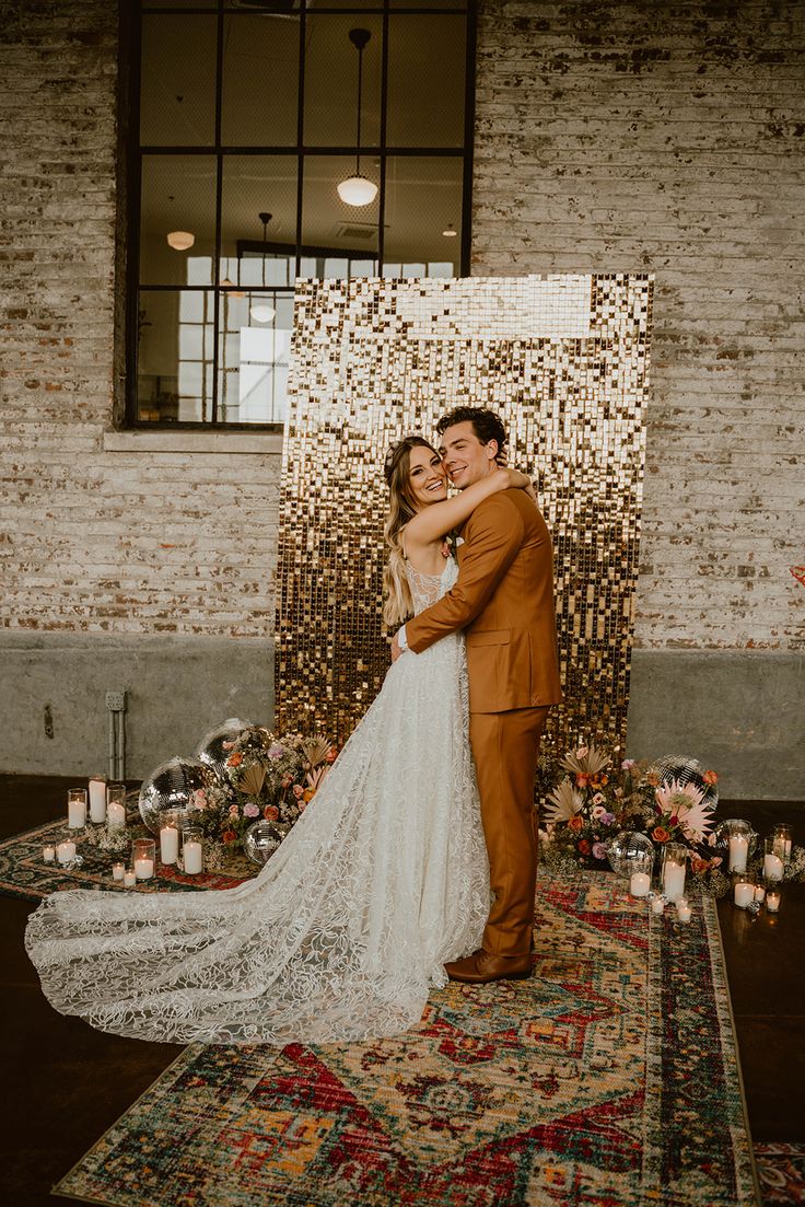 a boho wedding ceremony space with a gold sequin backdrop, pillar candles, disco balls, bright fresh and dried blooms