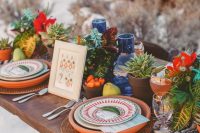 a bold boho wedding tablescape with terracotta plates, potted succulents, red blooms and blue candleholders plus woven chargers