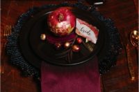 a bold place setting with black plates and a charger, a burgundy napkin and a gilded pomegranate