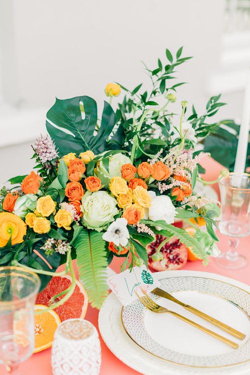 a bold summer wedding table with a pink tablecloth, bright blooms, greenery and tropical leaves and candles