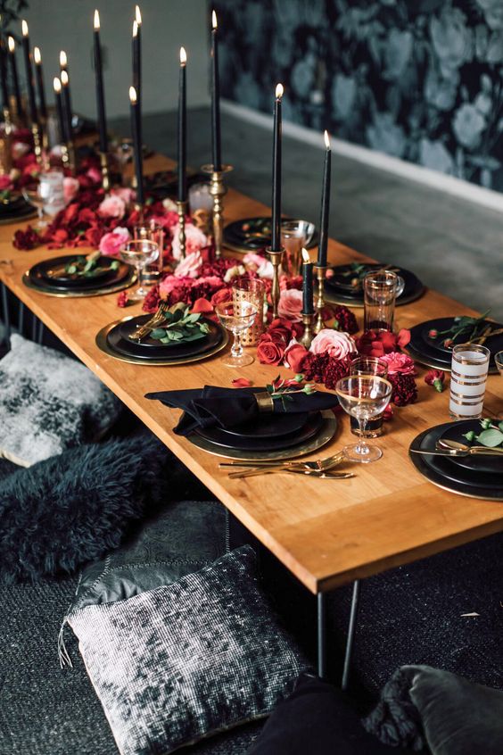 a bold wedding tablescape with black candles and plates, hot red and pink blooms on the table