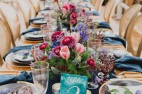 a bright and chic wedding tablescape with a navy runner and napkins, navy, pink and fuchsia blooms and lilac glasses