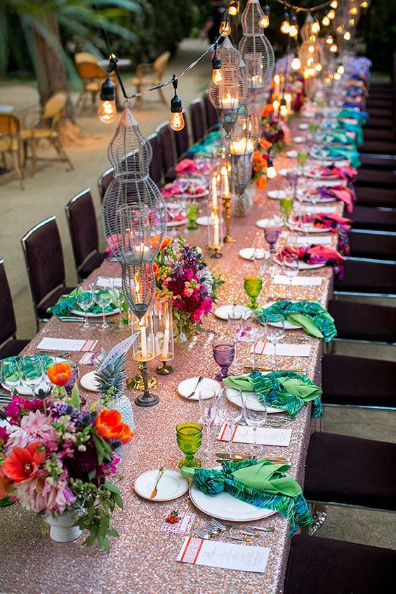 a bright festival wedding tablescape with a sequin tablecloth, printed napkins, colorful glasses, super bold blooms and candelabras
