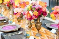 a bright wedding tablescape with an orange chevron table runner, hot pink menus, yellow, hot pink, orange and fuchsia blooms