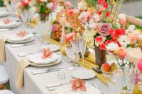 a cheerful wedding tablescape with dusty pink, red, yellow blooms and greenery, pale yellow napkins and a mustard runner