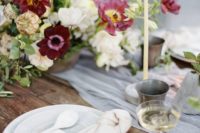a chic tablescape with a grey table runner, bold burgundy and neutral blooms and tall candles