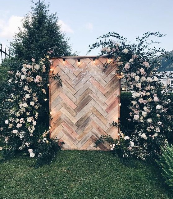 a chic wedding backdrop built of pallet wood clad with a herringbone pattern, lights and lush florals and greenery around
