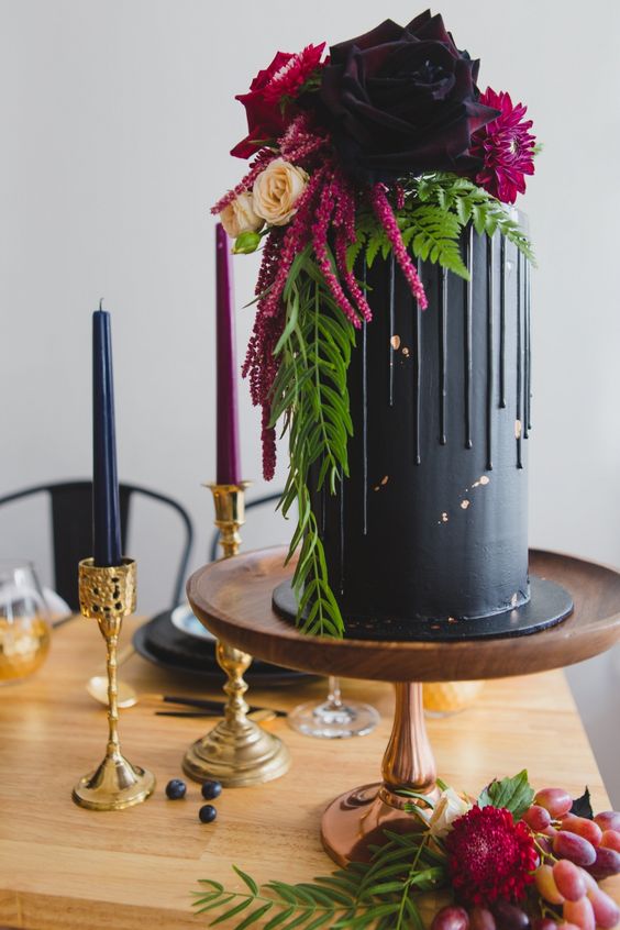 a chic wedding cake in black with drip and with hot red and pink blooms on top