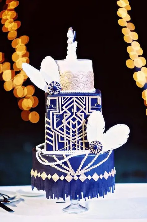 a cobalt blue and white wedding cake with rose scallops, beads, feathers and vintage brooches