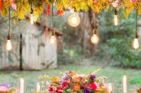 a colorful boho wedding tablescape with a green tablecloth, hot pink, purple and orange blooms and fern leaves, candles and gold touches