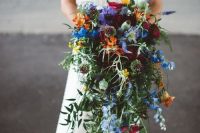 a colorful cascading wedding bouquet with blue, purple, burgundy and orange and yellow blooms and greenery is a gorgeous idea for a colorful wedding