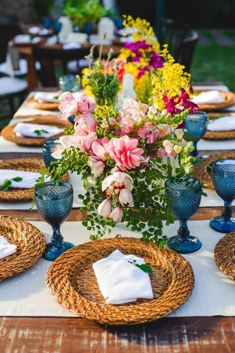 a colorful summer wedding tablescape with blue glasses, woven chargers, pink, hot pink and yellow blooms and greenery
