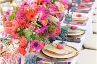 a colorful wedding table setting with hot pink and red blooms, purple and blue glasses, navy and pink napkins and greenery