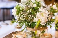 a cool rustic wedding centerpiece of a wood slice, jars with candles and jars with white blooms and greenery is chic