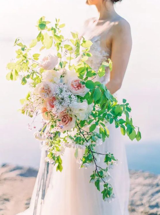 a creative textural cascading wedding bouquet with bold greenery and some blush peonies is a beautiful idea for spring or summer weddings