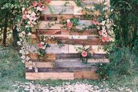 a cute pallet wedding backdrop with lush blooms and greenery plus petals all around looks very romantic