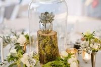 a glam woodland wedding centerpiece with moss, wood slices, blooms, a tree stump with a succulent in a cloche