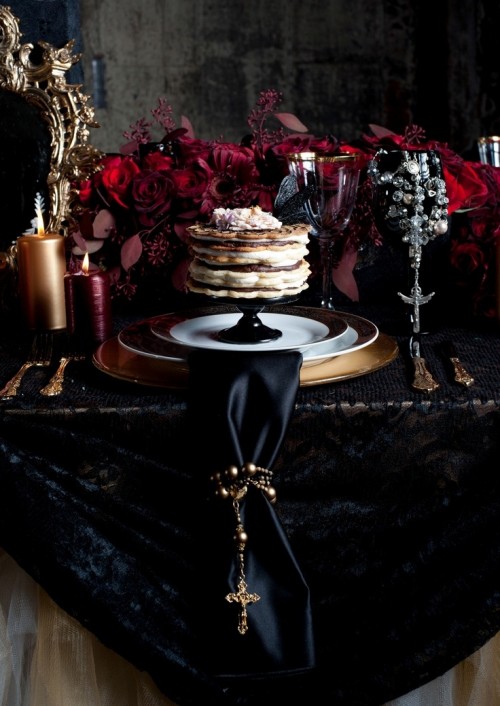 a gorgeous soft gothic wedding tablescape with a black lace tablecloth, a black napkin, gilded plates and lush deep red florals on the table