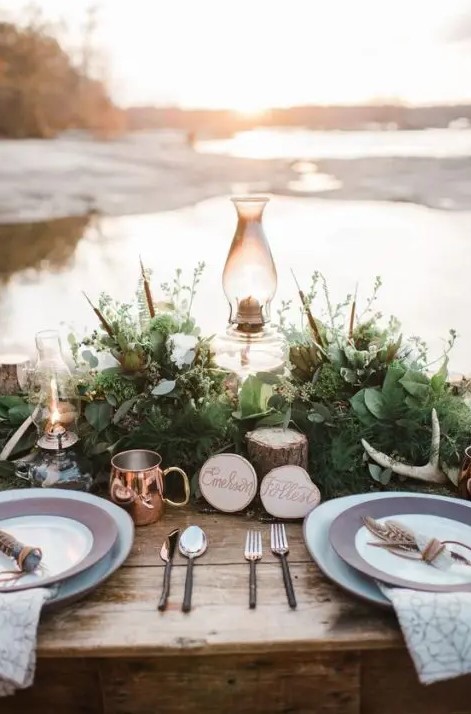 a gorgeous forest wedding tablescape with a lush greenery runner, antlers, stumps, lamps and copper touches
