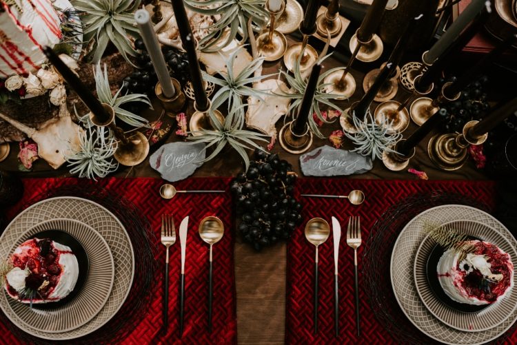 a gorgeous wedding tablescape done in red and black, with woven chargers, grapes, air plants, black candles and gilded touches