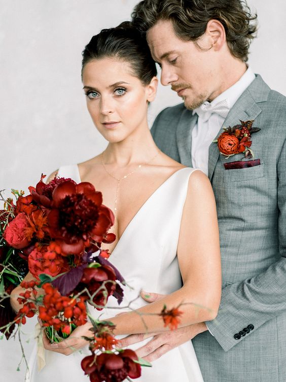 a grey suit, a white bow tie and a bold rust and burgundy floral boutonniere for a trendy and modern groom's look