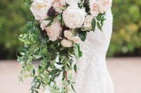 a jaw-dropping cascading wedding bouquet of white and blush roses and peonies, some deep purple blooms and greenery is a wow solution