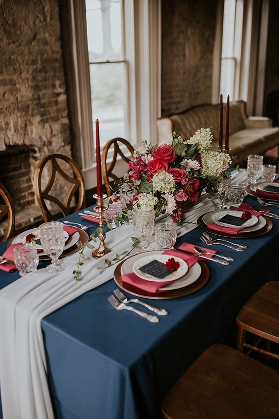 a lovely wedding tablescape with a navy tablecloth, pink napkins, pink and white blooms, navy menus and deep red candles