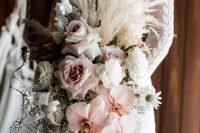 a lush and luxurious cascading wedding bouquet with white and blush roses, orchids, ranunuculus, pampas grass and pale leaves is wow