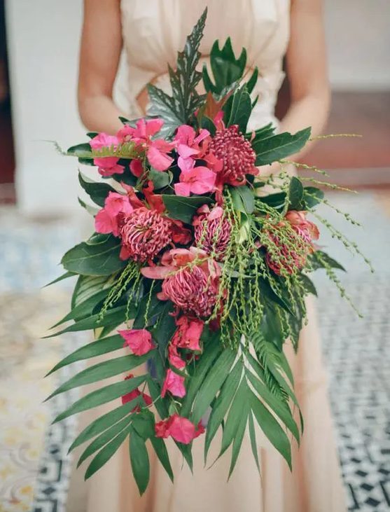 a lush cascading tropical wedding bouquet with much greenery and pink flowers of various kinds