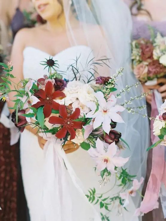 a lush tropical cascading bouquet with large burgundy and white blooms, thistles and greenery