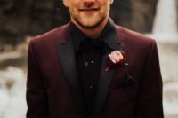 a maroon wedding suit with black lapels, a black shirt and bow tie for a statement wedding look