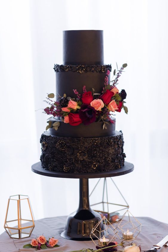 a modern black wedding cake with textural tiers, red and peachy flowers for decor