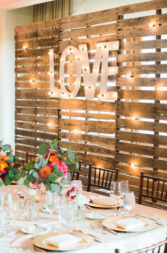a pallet backdrop with lights and large marquee letters is a nice idea for the wedding venue backdrop