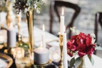 a refined wedding tablescape with a graphite grey table runner, bold red and burgundy blooms, gilded candleholders and greenery