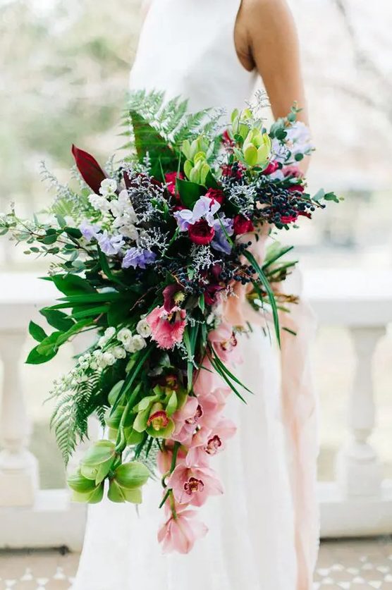 a romantic colorful cascading wedding bouquet with pink, purple and red blooms plus much greenery for a tropical wedding