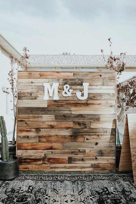 a rustic boho wedding backdrop made of stained pallet wood and monograms plus cacti around is a trendy idea