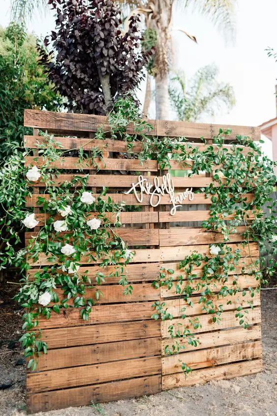 a rustic wedding backdrop of wood, with greeneyr and white blooms plus calligraphy is a great idea for a rustic wedding
