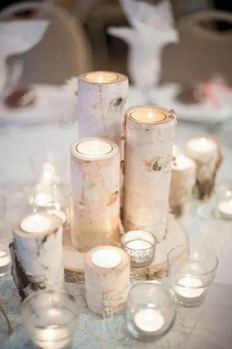 a simple and cozy winter wedding centerpiece of candles in glass and branch candleholders on a wood slice