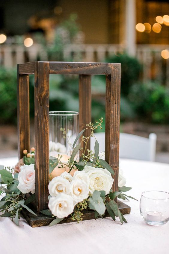 a simple and elegant wedding centerpiece of a wood frame with a candle and white and blush blooms and greenery for a rustic wedding