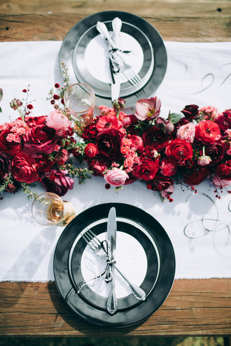 a stylish tablescape done with lush red and pink blooms, a white runner and black and white plates and chargers