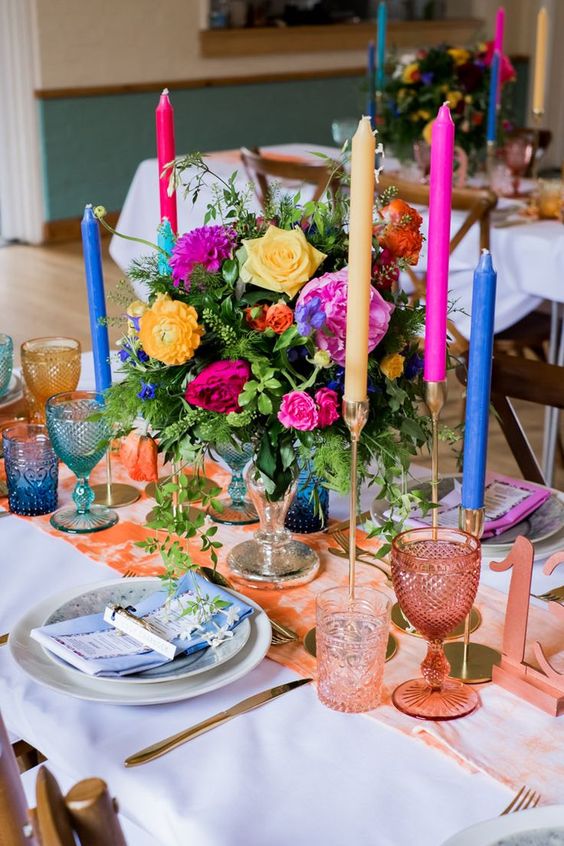 a sumptuous wedding tablescape with a peachy runner, glasses and a table number, navu, fuchsia candles, yellow and hot pink blooms