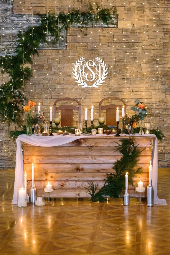 a sweetheart wedding table covered with wood, with a fabric table runner, candles, an evergreen runner and blooms is a lovely idea