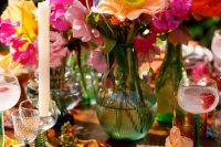 a vibrant wedding table setting with red, hot pink, orange blooms and greenery, candles, blush plates and glass candleholders