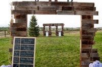 a wedding gate built of stained pallets with monograms and a chalkboard sign plus blooms in buckets
