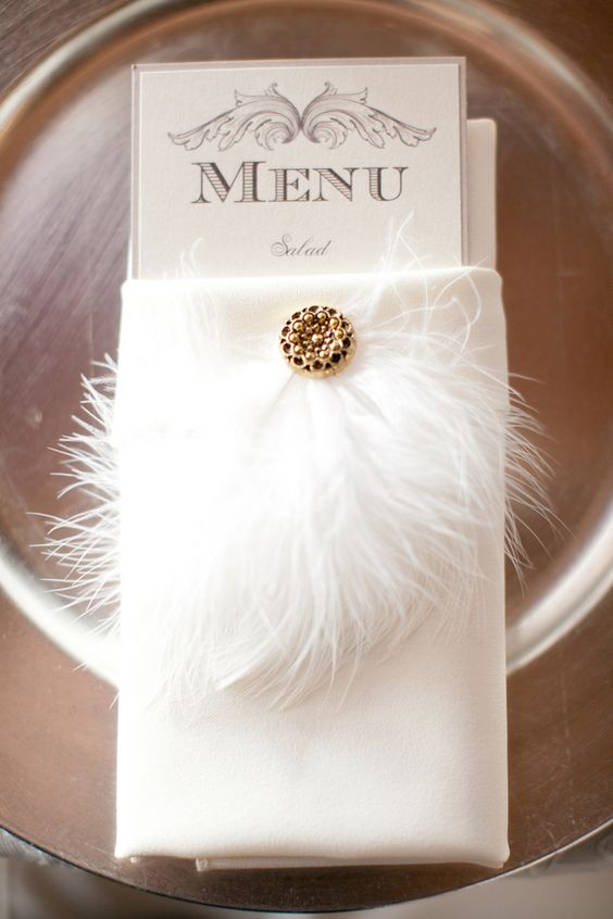 a wedding menu decorated with feathers and a brooch is a gorgeous idea for a chic wedding