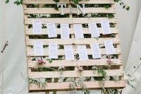 a wedding seating chart with a pallet on stands and monograms and much greenery
