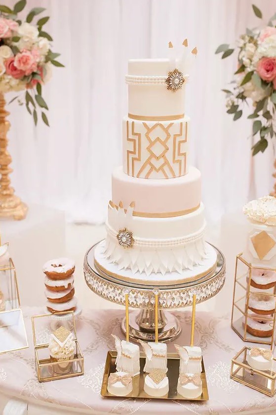 a white and gold wedding cake with geo decor, petals, beads, feathers and vintage brooches
